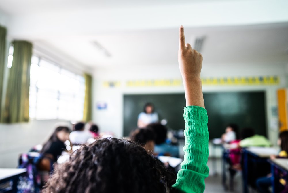 Students' raised hands in a classroom.