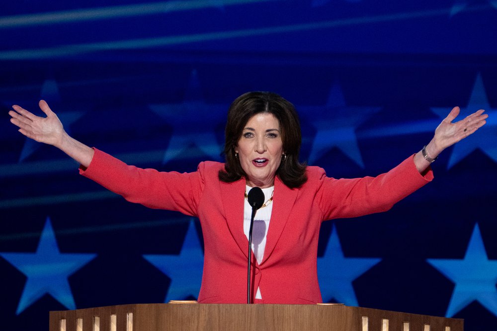 New York Governor Kathy Hochul stands at a podium with her arms spread wide.