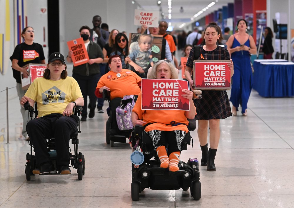 Protesters in wheelchairs carry signs reading "Home care matters to Albany"