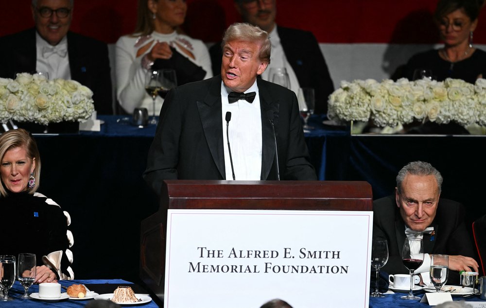 Former President Donald Trump speaks at a podium that says The Alfred E. Smith Memorial Foundation. Senate Leader Chuck Schumer sits next to him