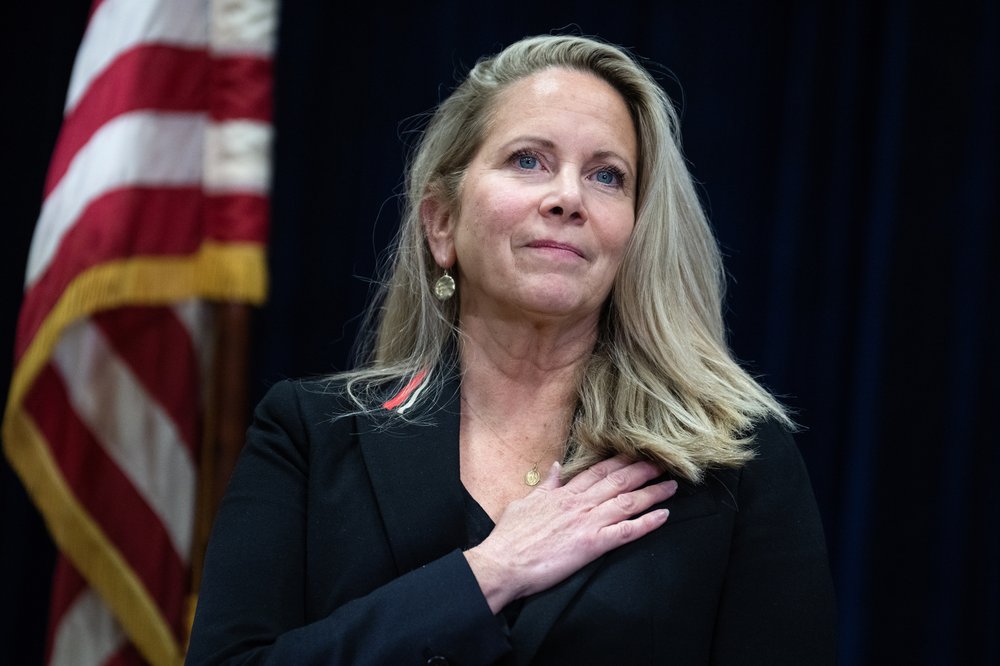 Laura Gillen with a hand on her heart and an american flag behind her