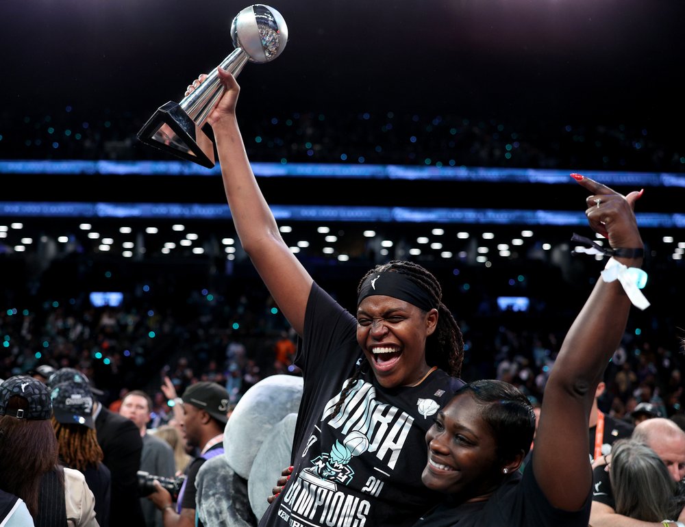 Jonquel Jones of the New York Liberty holds up her MVP trophy while celebrating a Game Five win with her fiancée.