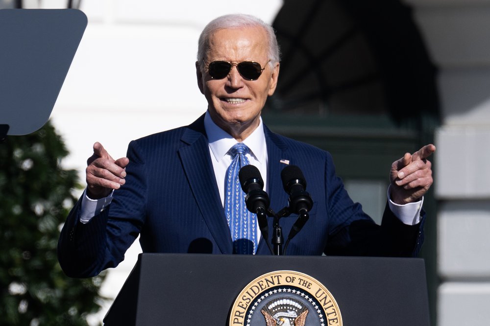 President Joe Biden smiles and points from behind a podium with the presidential seal.