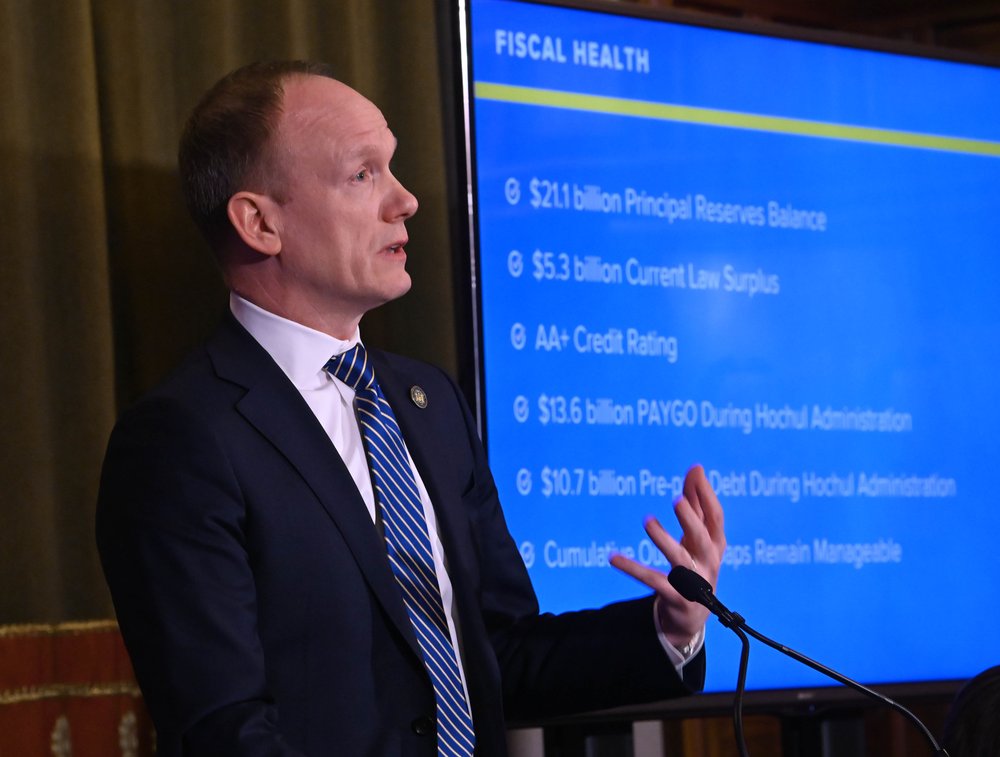 A man in a suit delivers a budget briefing at a podium.
