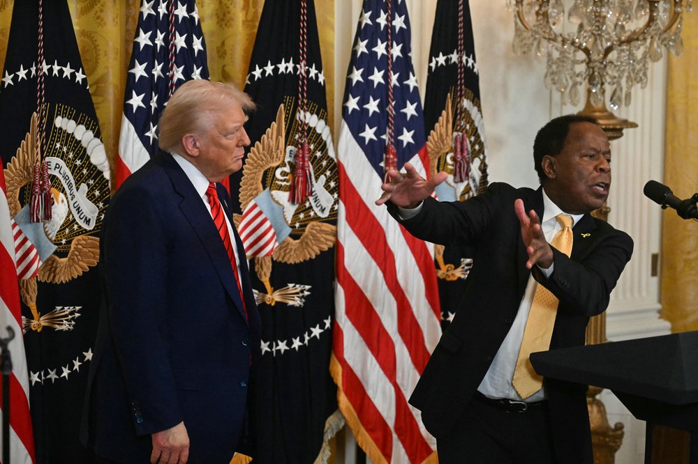 A man speaks at a podium beside President Trump.