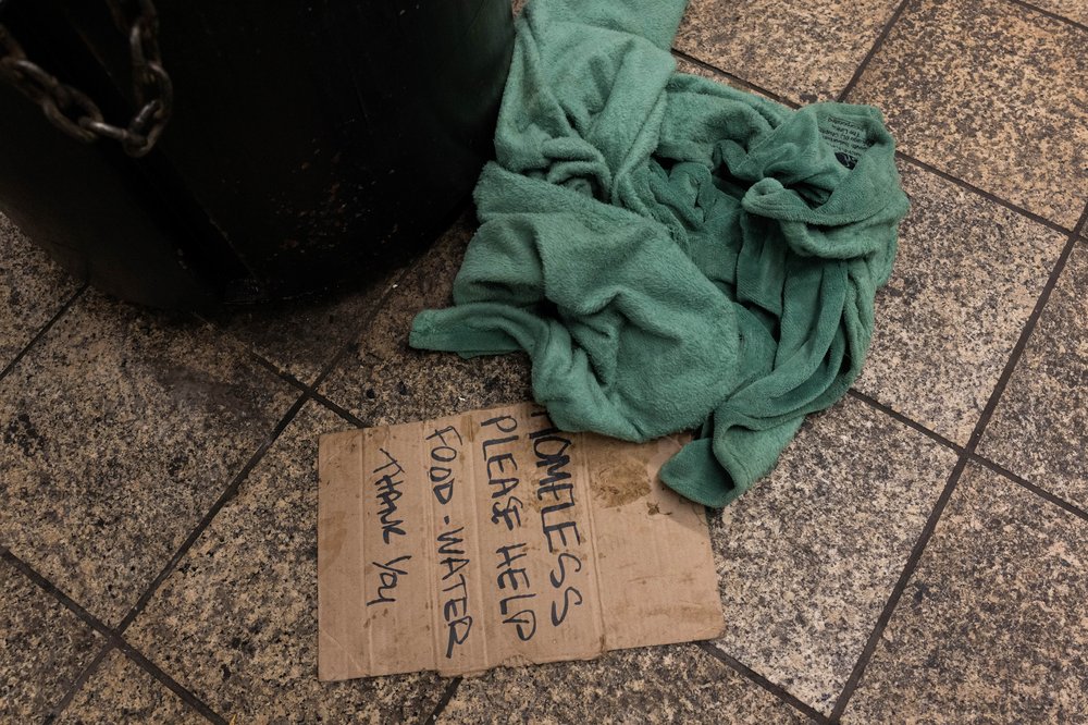 A cardboard sign on the ground says "homeless please help food - water thank you"