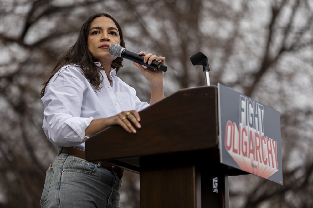 Alexandria Ocasio-Cortez in a white shirt and jeans at a podium