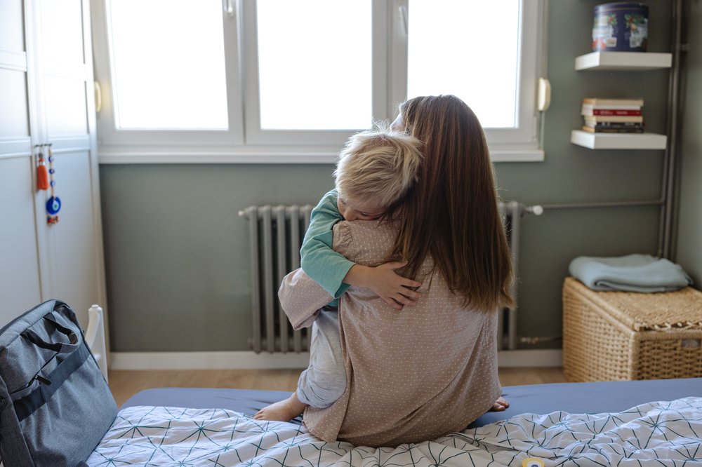 A mother embraces her child while seated on a bed in a peaceful bedroom environment.