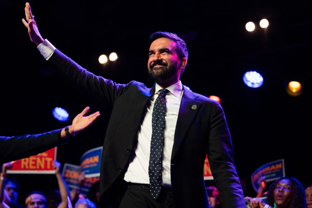 Zohran Mamdani waves on a stage.