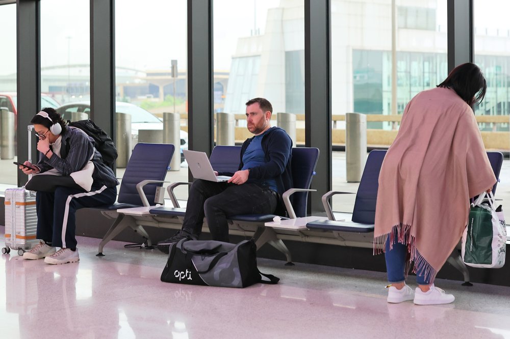 A group of grumpy travelers at Newark Airport. A man sits at a laptop. He looks pretty angry. Another woman is wrapped in a blanket. She's getting ready to settle in for a long delay, perhaps.