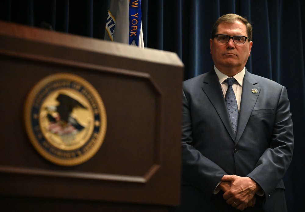 A man in a suit stands by a Department of Justice podium.