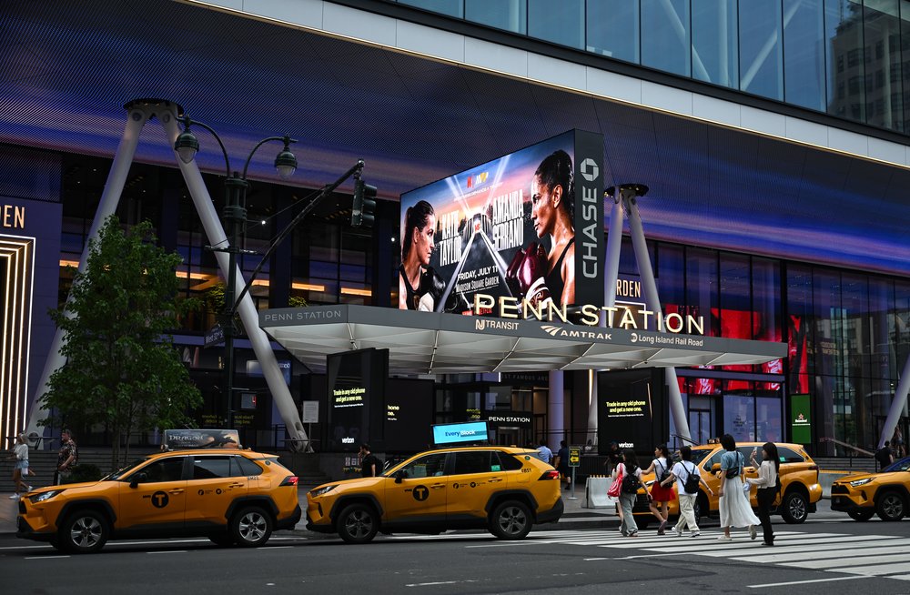 Yellow taxis linger in front of a big old sign that says PENN STATION.
