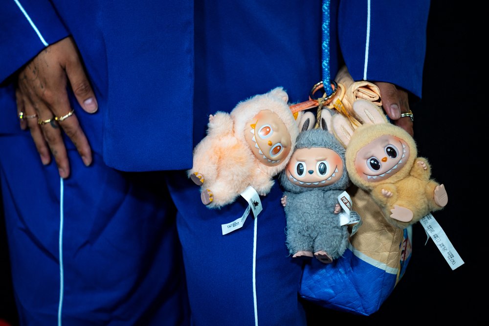 A person wearing royal blue is wearing three small stuffies called Labubus.