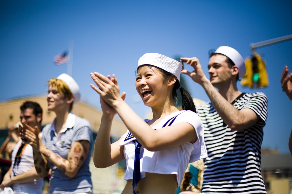 A man and a woman dressed as sailors applaud outside.