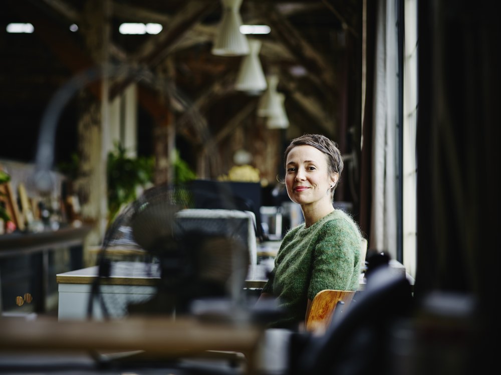 A woman in a green sweater sits in a desk at work.