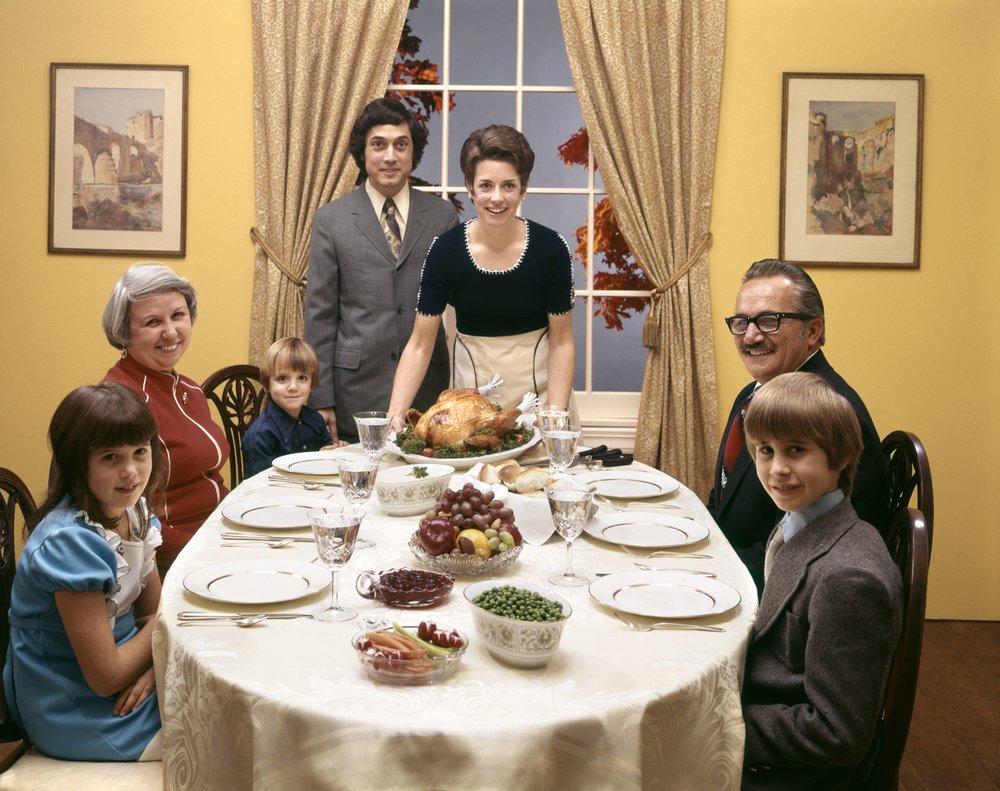 A family stands around a table set for Thanksgiving.