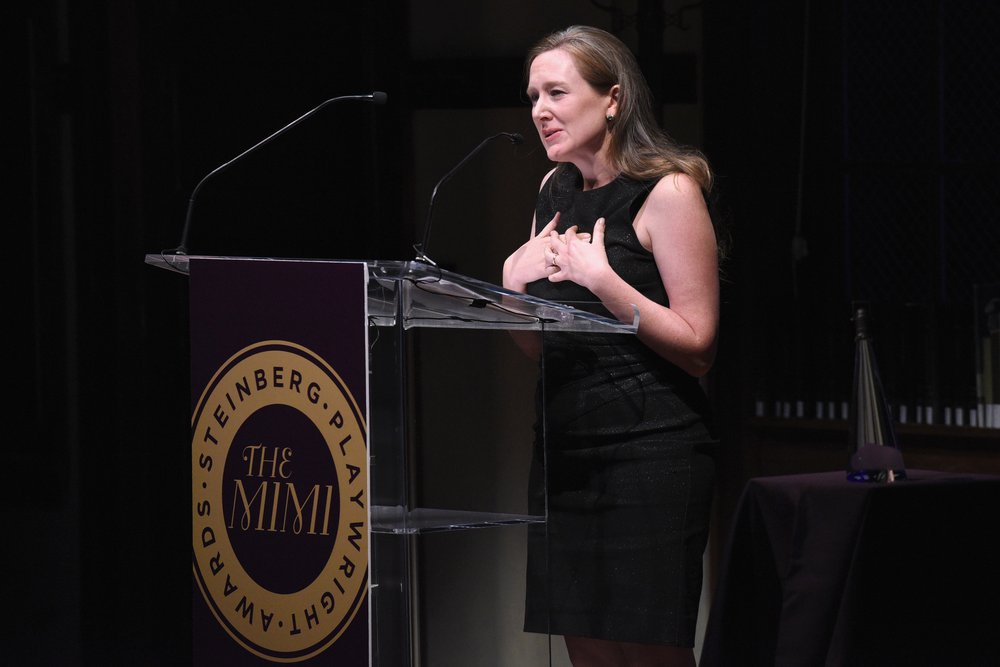 A woman speaking at a lectern in a dark room.