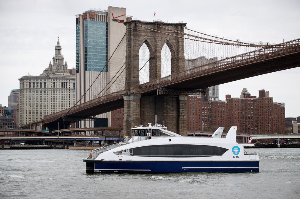 A photo of an NYC Ferry boat beneath the Brooklyn Bridge.