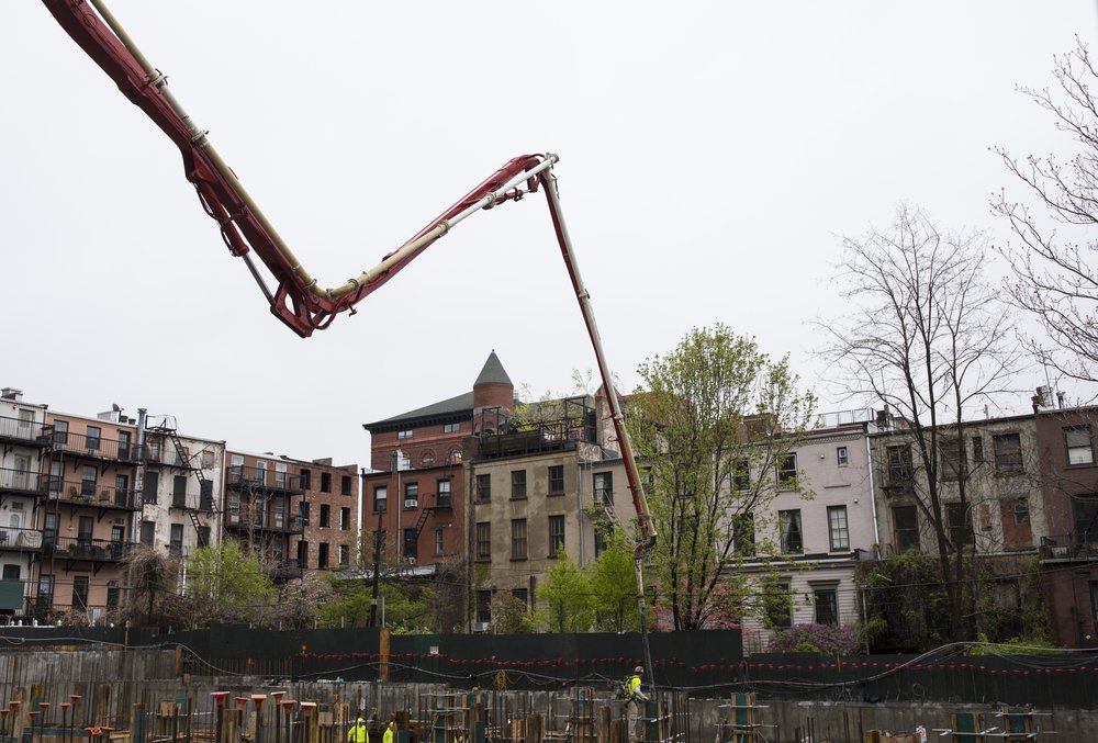 A pipe pumping concrete into a building foundation towers over residential brownstones in Brooklyn.