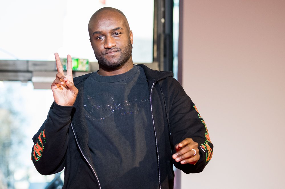 A man wearing a black hoodie flashes a peace sign at the camera.