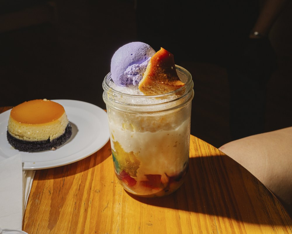 A colorful dessert in a cup, made up of condensed milk, and topped with a scoop of purple ice cream.