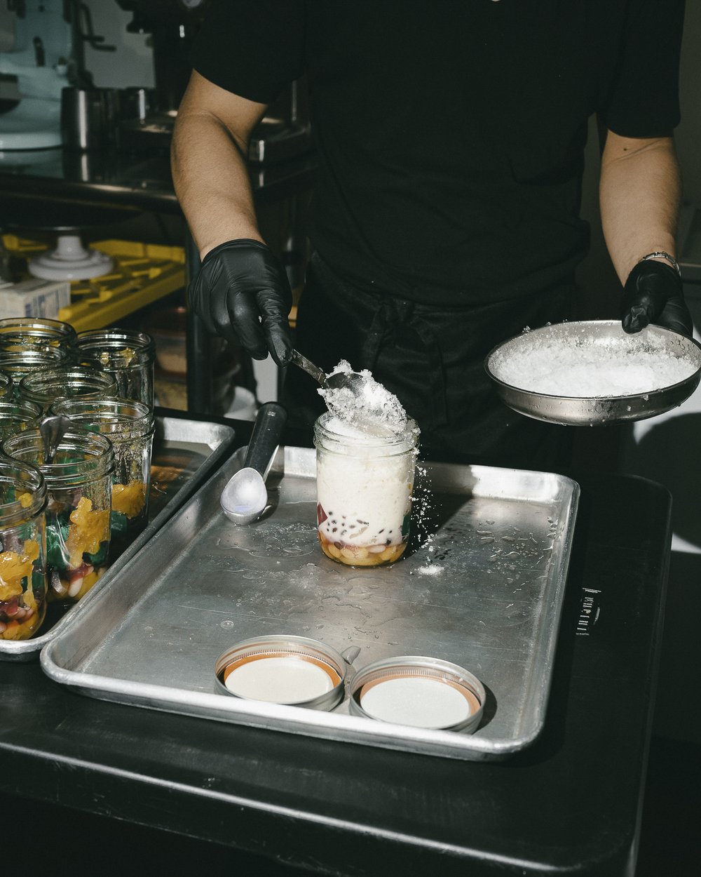 A hand sprinkles shaved ice over an open cup, filled partially with milk.