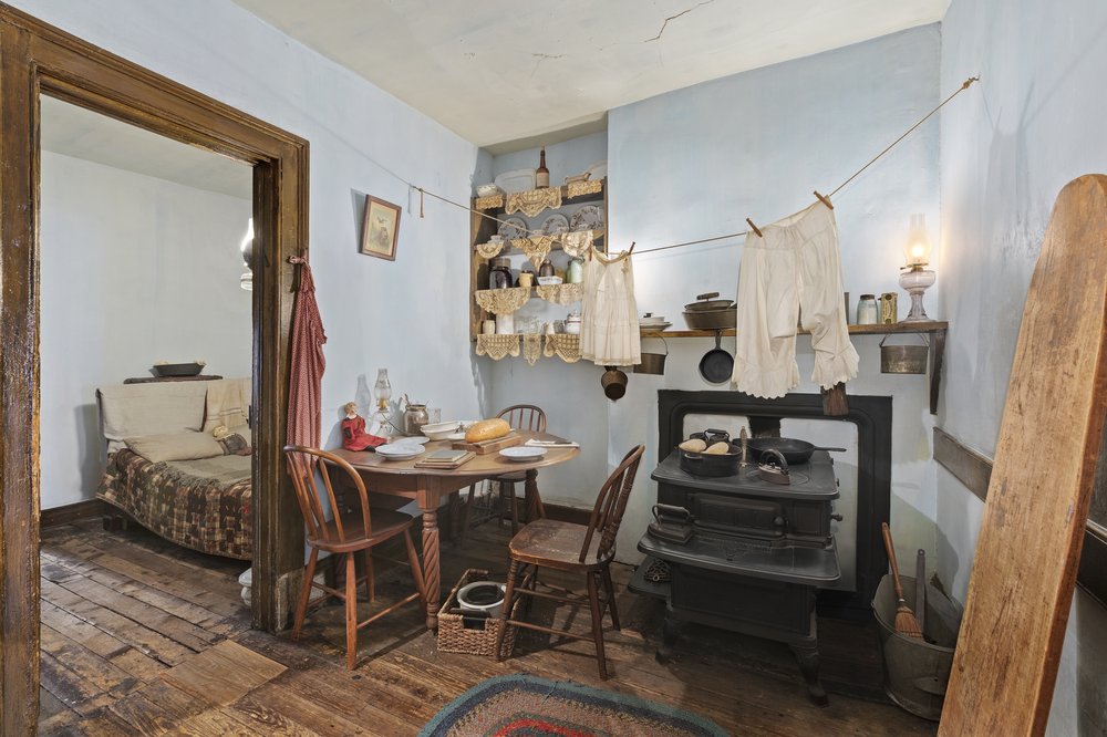 A room with an old stove and under garments hanging on a string to dry.