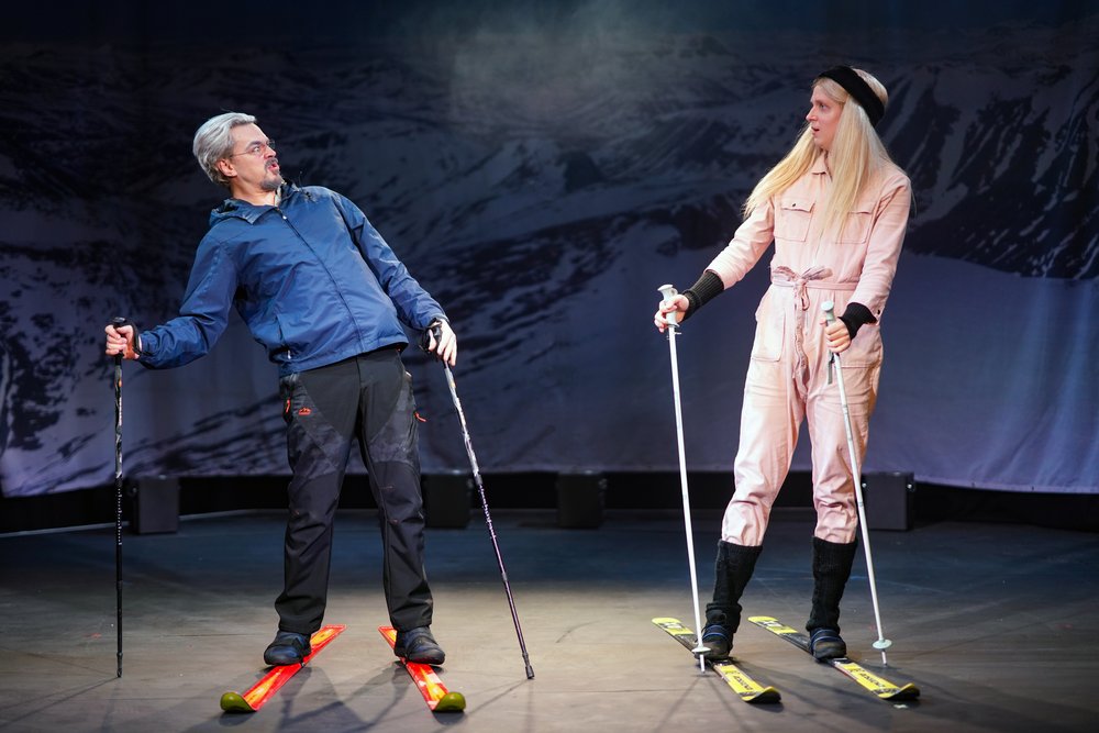 Two actors on skis look at each other.