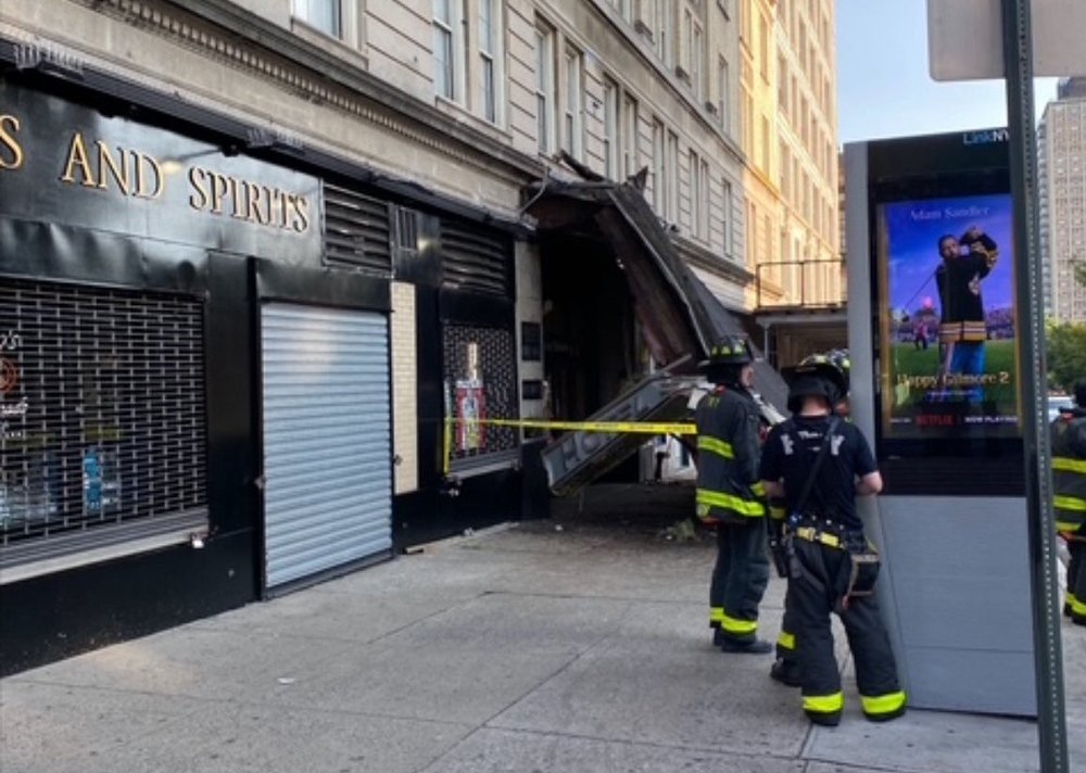 An awning that fell down above a Brooklyn subway station. Firefighters stand near by.