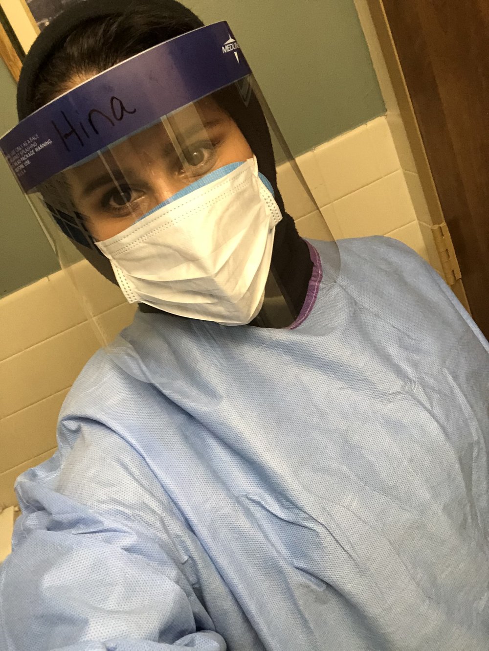 Hina Naveed, a brown-skinned woman originally from Pakistan, wears a surgical mask and face covering.
