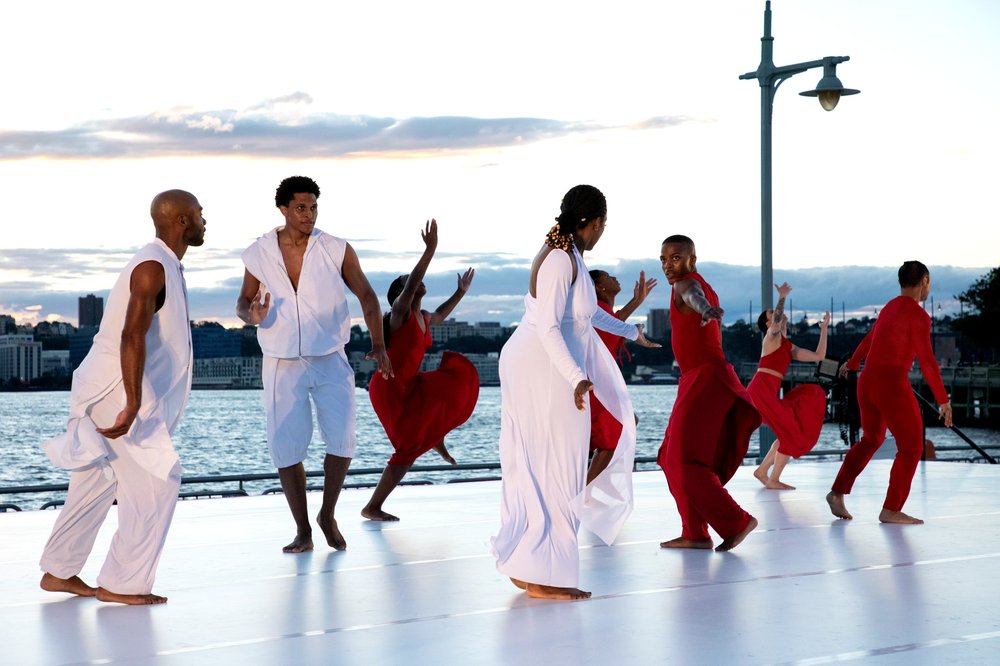 Dancers on an outdoor stage with a river behind them.