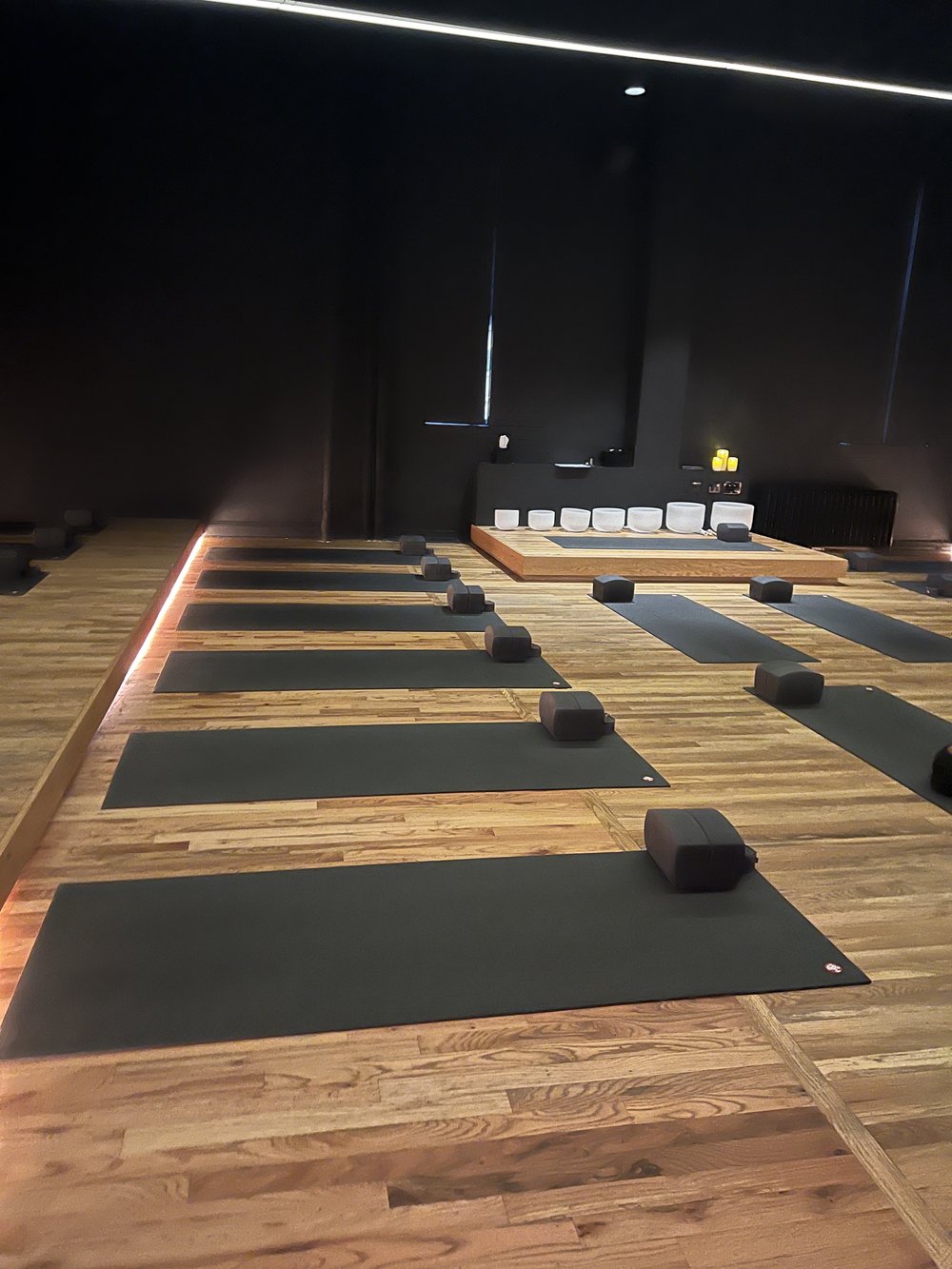 An expansive room with hardwood floors, yoga mats, and white sound bath jars.