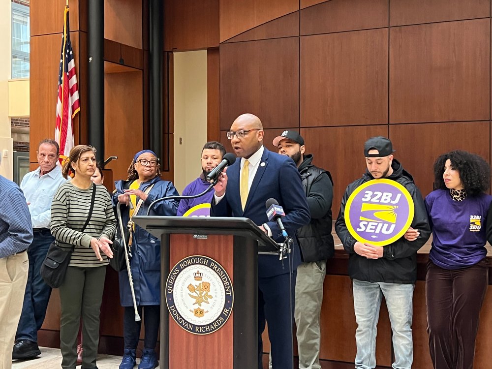 Queens Borough President Donovan Richards surrounded by other people at podium.