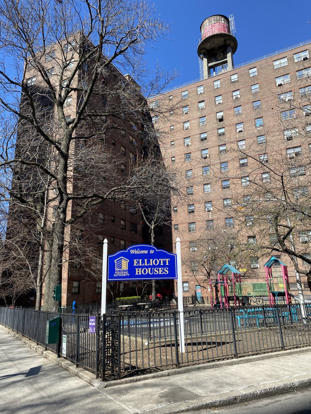 A photo of the Elliot Houses in Chelsea, a large brick building with a water tower and playground.