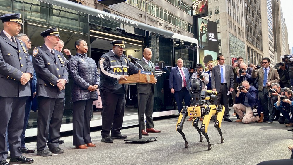 Mayor Eric Adams and top NYPD brass gaze upon a robotic yellow dog in Times Square.