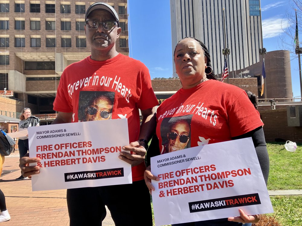 Ricky and Ellen Trawick, holding signs saying to fire the two officers involved in their son's death, wear red shirts with a photo of Kawaski.