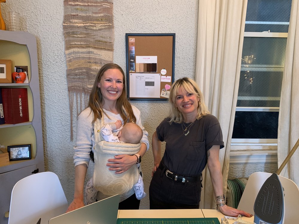 Two women in an apartment, one of whom is wearing a baby