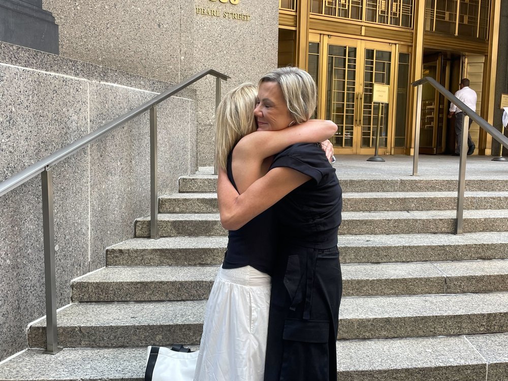 Two women embrace on the steps of a courthouse.