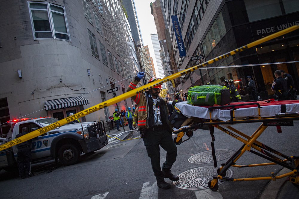 A paramedic pulls an ambulance cot under police taper at the scene of a building collapse.