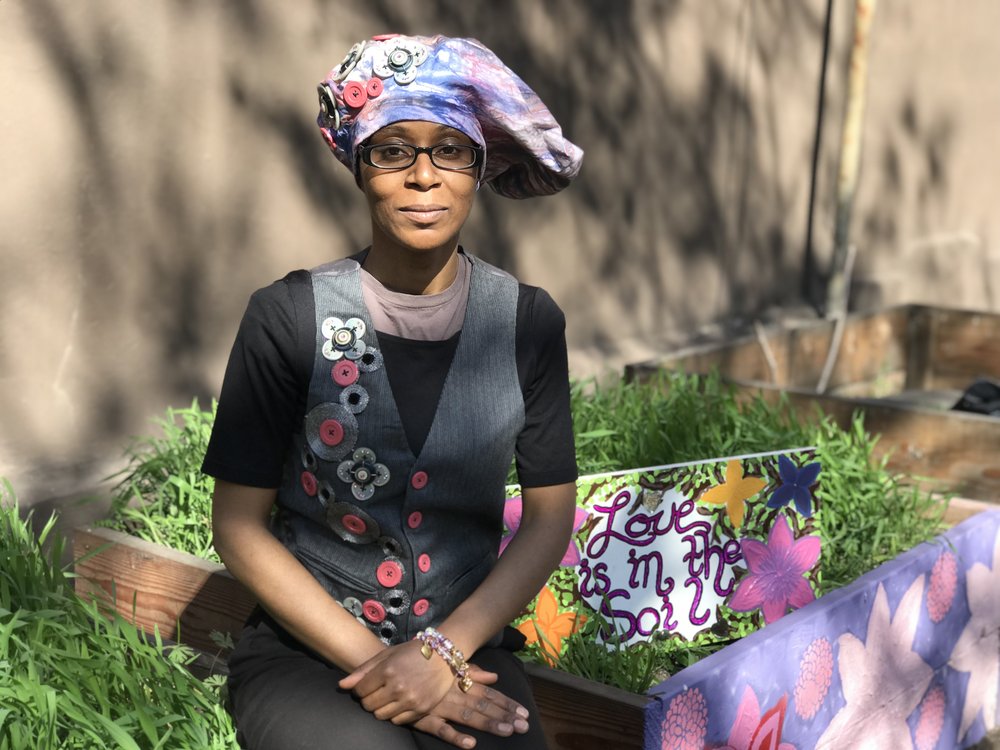 community gardener Nadege Alexis sitting on a colorful flower bed with sun shining on her face.