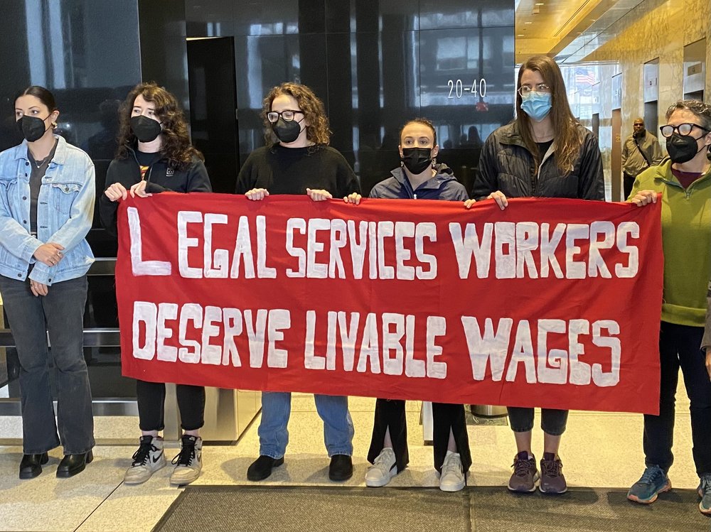 Staff at Mobilization For Justice protest while holding a sign.