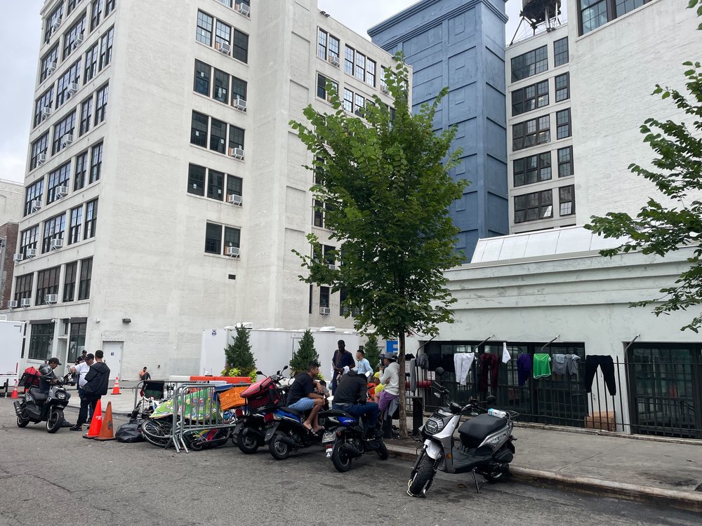 A large building in Brooklyn with e-bikes and mopeds parked in front.