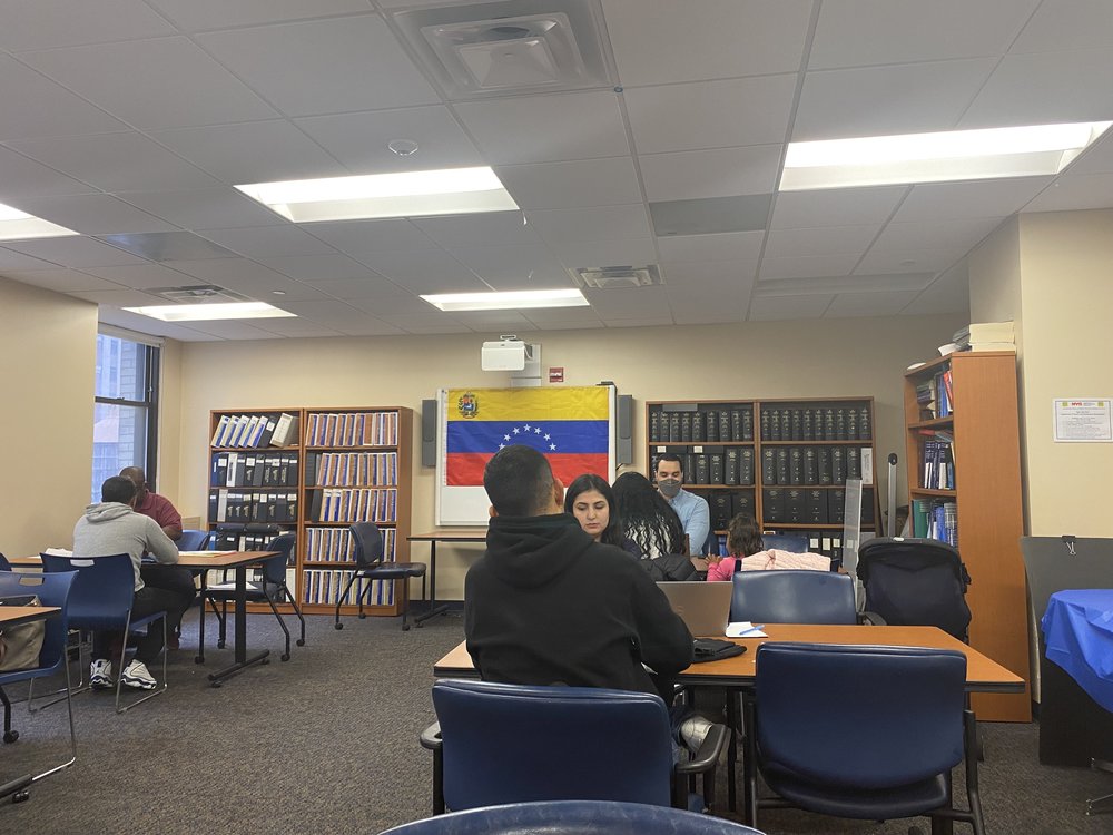 A Venezuelan flag hangs off of a board while people sit around tables during a TPS clinic