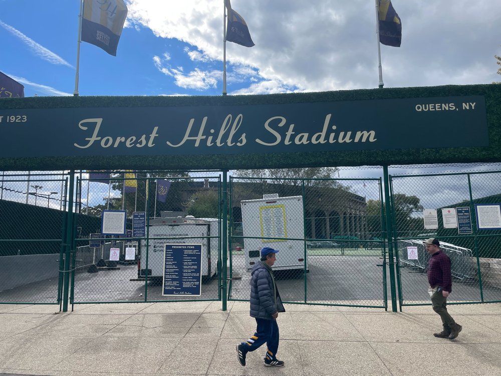 The gate of the Forest Hills Stadium, where two people are walking past the fences.
