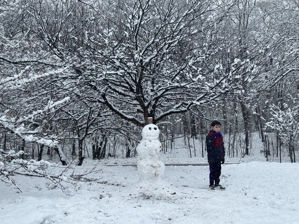 A kid stands next to a snowman in Prospect Park.