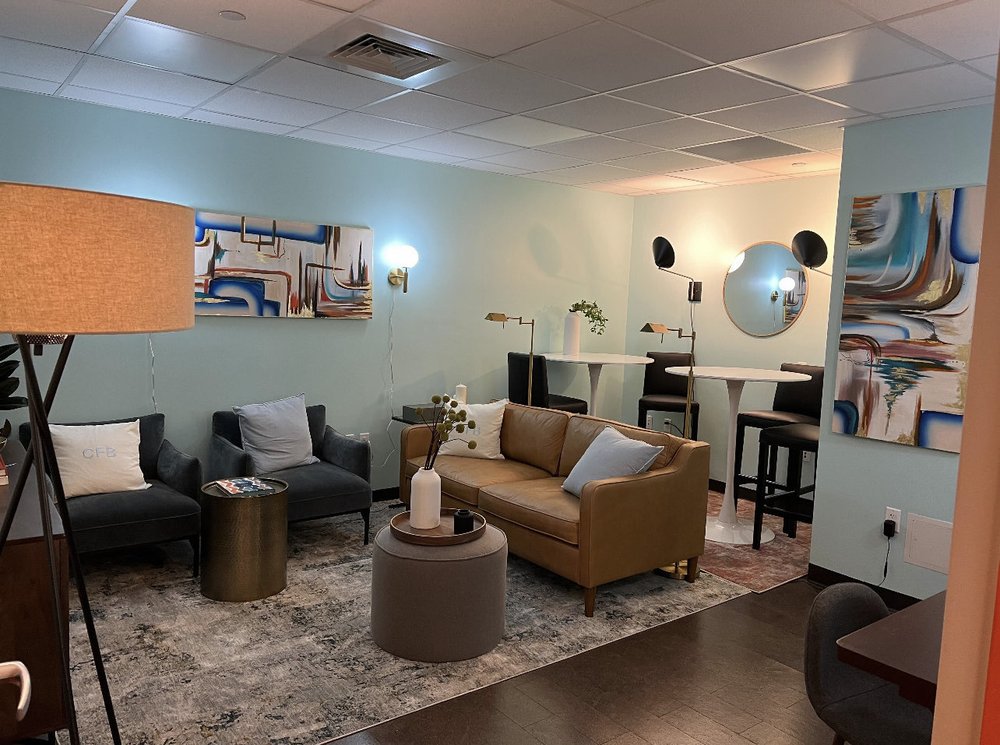 The newly upgraded staff lounge at the New York City Campaign Finance Board shows modern furniture, including a tan couch, two chairs, high-top tables and abstract art.