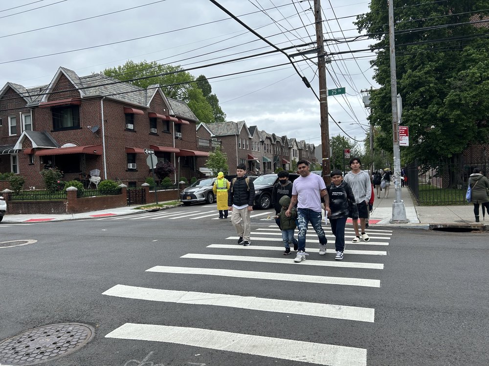 Kids cross the street with a crossing guard in the background.