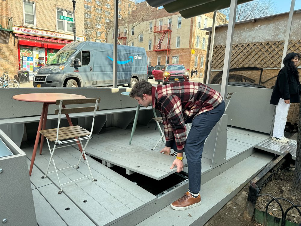 A man lifts up a floor panel of an outdoor dining shed.