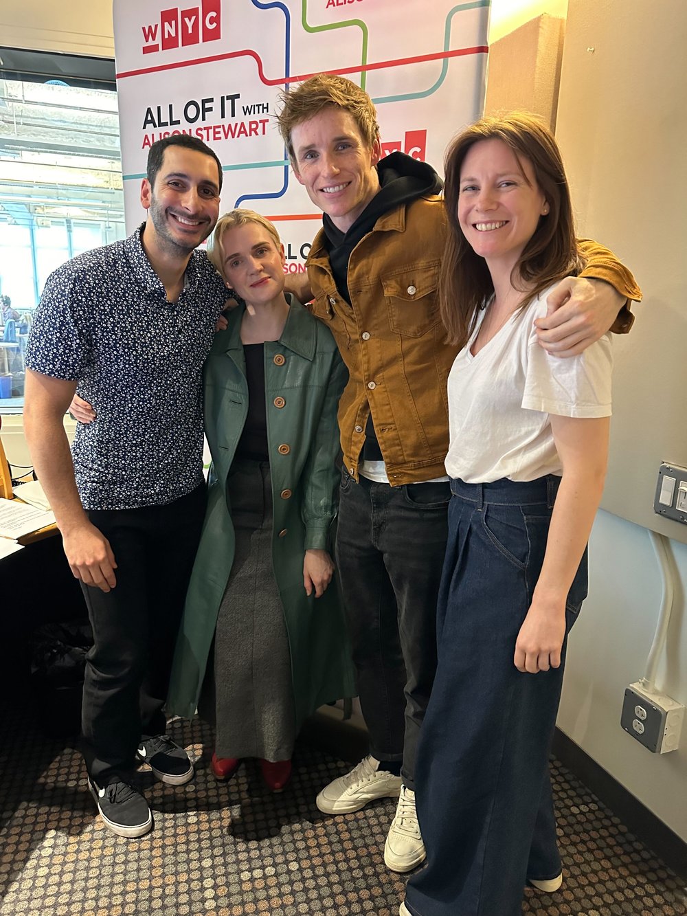 A group of four people stand together with their arms around each other.