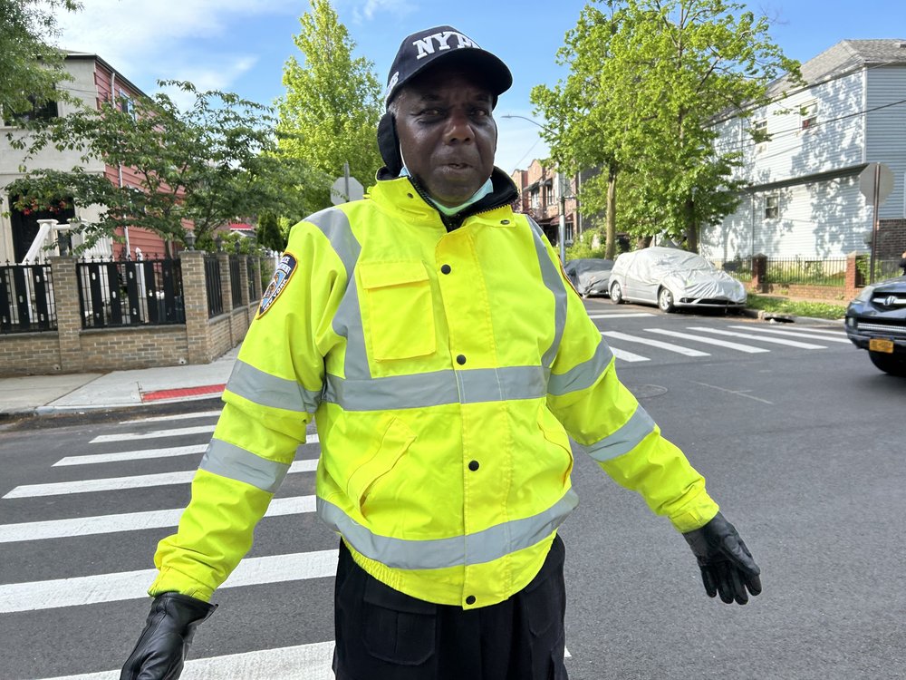 A man in a yellow windbreaker and NYPD hat at an intersection.